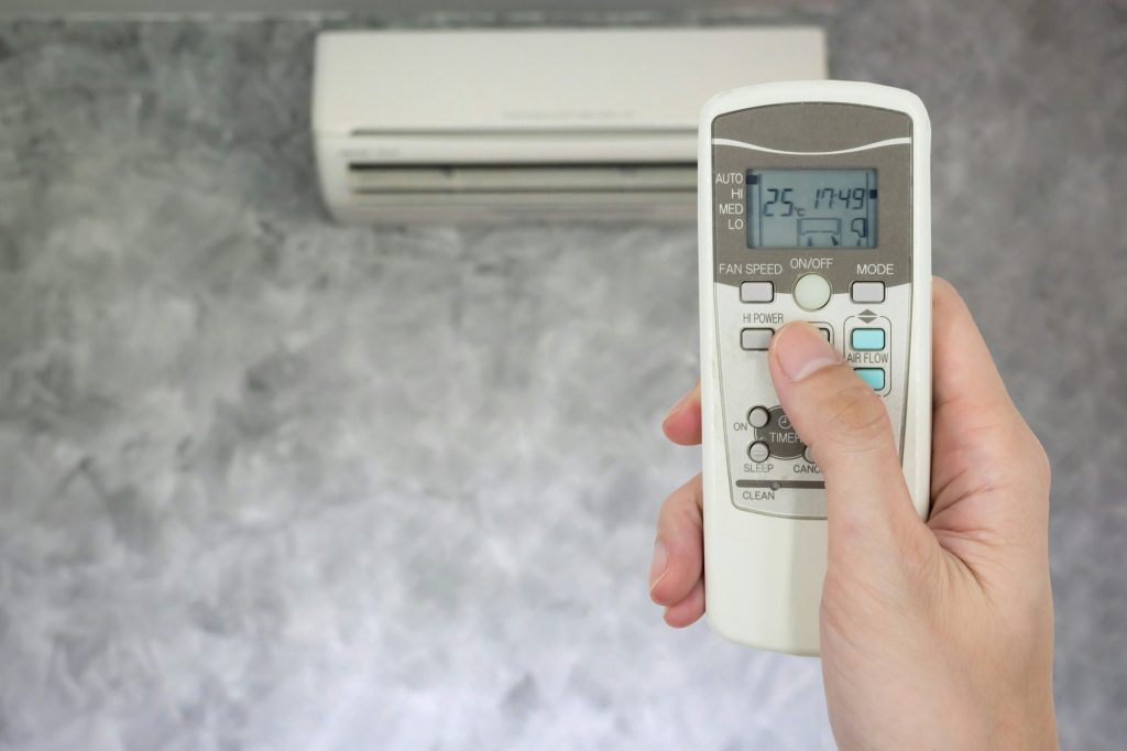 Hand holding remote in front of air conditioner.